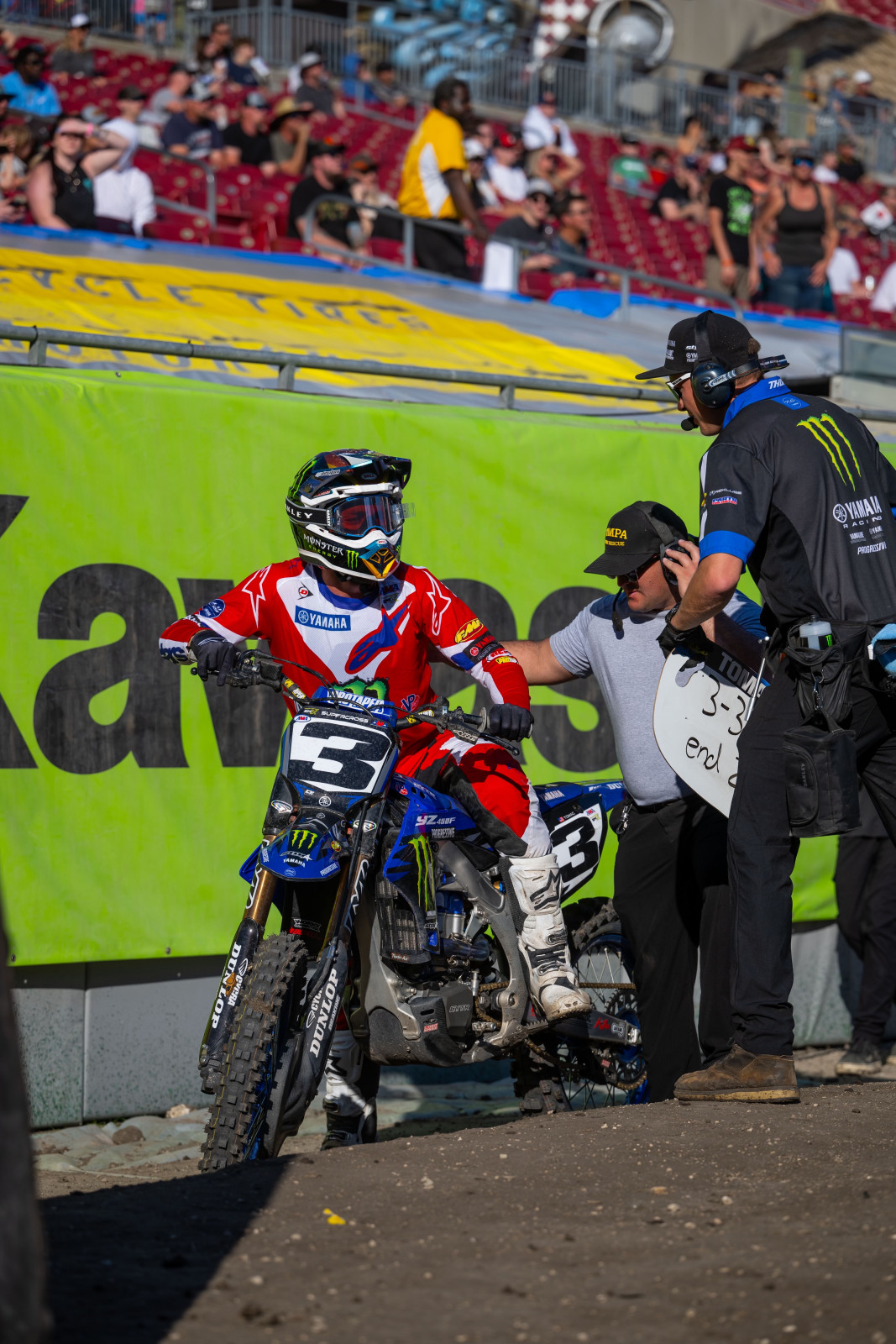 Eli Tomac talking with team personnel after dabbing his left leg in a turn.