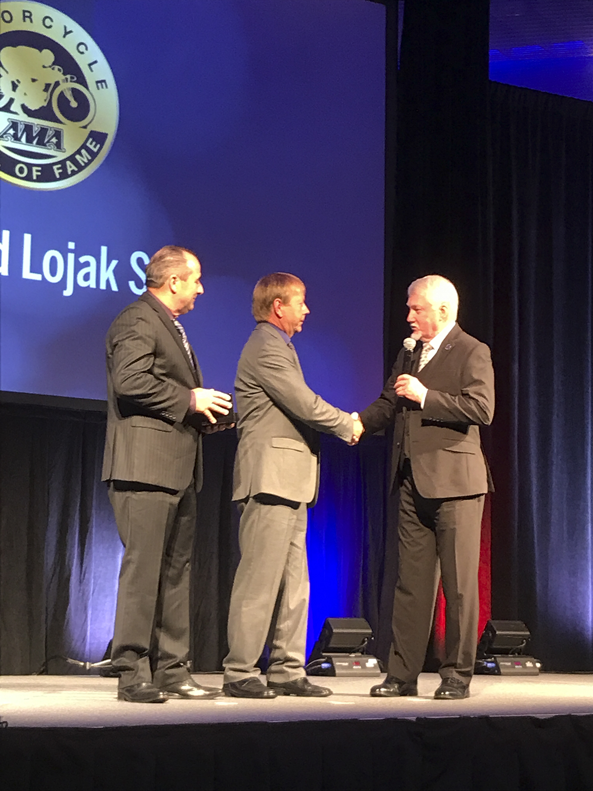 Ken Sutton shakes Ed Lojak's hand as fellow AMA Motorcycle Hall of Fame Scot Harden looks on.